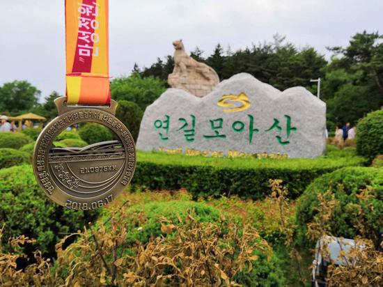 A finishers' medal is displayed in front of the Mao'er Mountain National Forest Park of Yanji. （Photo/chinadaily.com.cn）