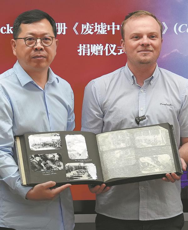  Oscar Lebeck holds up his father's photo album with Wu Chongqing of Sun Yat-sen University on July 4. [Photo provided to China Daily]