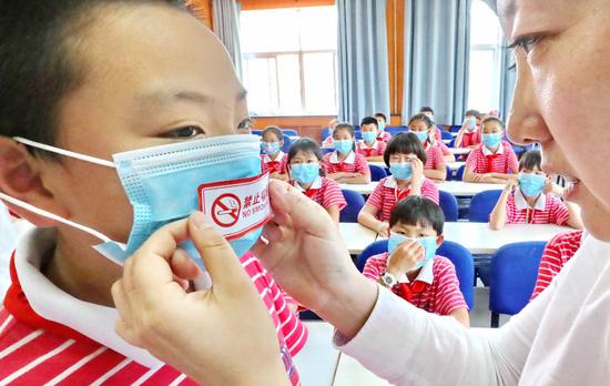 A social worker places a no-smoking sticker on the mask of a primary school student in Qinhuangdao, Hebei Province, on Wednesday, ahead of the World No Tobacco Day, which falls on Thursday.  (Photo provided to China Daily)