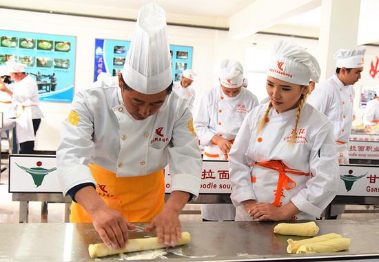 A chef shows a student how to flatten dough using a rolling pin at the school. (Photo: Xinhua/Wang Peng)