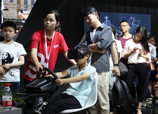 A young visitor experiences simulated driving on a virtual reality or VR headset at the stand of Manbang Group, at the 2018 International Big Data Industry Expo held in Guiyang, Guizhou province, on May 26.(Photo by Yang Jun/China Daily)