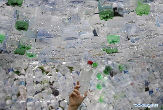 A person poses for a picture adding a plastic bottle to the work the Space of Waste, an art installation highlighting the problem of plastic pollution, at ZSL London Zoo in London, Britain on May 24, 2018. The work, by artist and architect Nick Wood, is 16 feet high and is made from 15,000 discarded single use plastic bottles collected from London and its rivers. (Xinhua/Tim Ireland)
