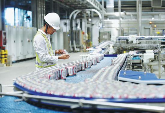 An employee inspects beer cans just before they are dispatched from AB InBev's Putian plant in Fujian province last year. (Photo provided to China Daily)