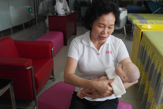 Liu Guixiang demonstrates the proper way to feed an infant using a model at her training center in Jinan, East China's Shandong province. (Photo/chinadaily.com.cn)
