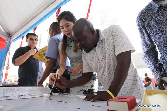 A Chinese teacher from Confucius Institute of Dodoma University teaches a local man to write Chinese calligraphy during an exhibition to commemorate the Chinese New Year in Dar es Salaam, Tanzania, Feb. 9, 2018. (Xinhua)