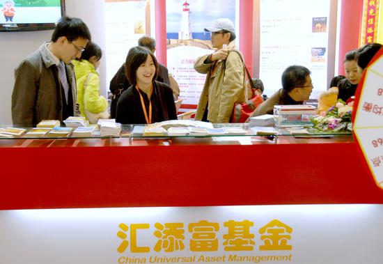 A fund manager from an asset management company oversees brochures about various financial products, to be given away to prospective individual investors, at the company's stall at the 7th Money Fair held in Shanghai earlier this year. （Photo provided to China Daily）