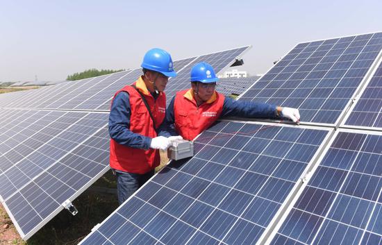 Technicians check panels at a solar power plant in Mingguang, Anhui Province, on April 25. (Photo by Song Weixing/For China Daily)