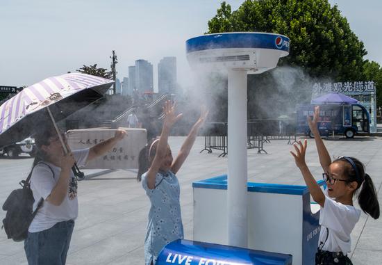 People cool off with a misting system set up in Chenyi Square at the Bund in Shanghai as the high reached 37 C on Tuesday. Rains are expected to bring relief on Thursday. (WANG GANG/CHINA DAILY)