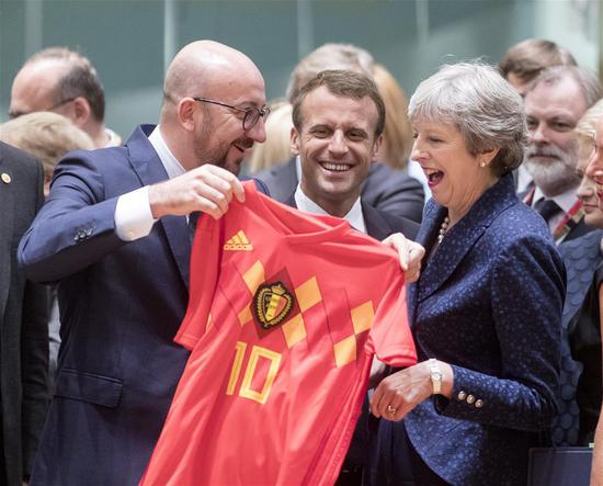 Belgian Prime Minister Charles Michel (L) offers a Belgian National Soccer team jersey to British Prime Minister Theresa May (R) as France's President Emmanuel Macron (C) looks on at the first day of a two-day EU Summit in Brussels, Belgium, June 28, 2018.(Xinhua/Thierry Monass)
