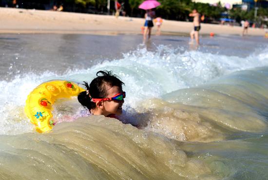 A child enjoys a cool moment in the ocean waves at a scenic zone in Sanya, Hainan Province, on Sunday. Several cities in the province have issued heat alerts recently. (Photo/
China Daily)