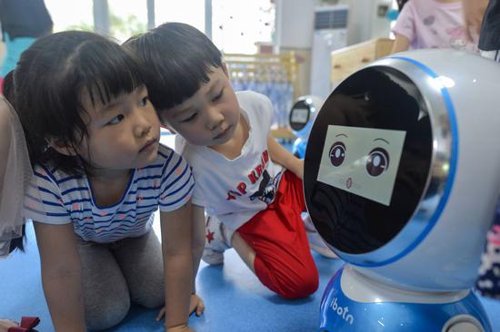 Children play with an intelligent robot at a kindergarten in Wuhan, capital of Hubei Province. (Photo by HU DONGDONG FOR CHINA DAILY)
