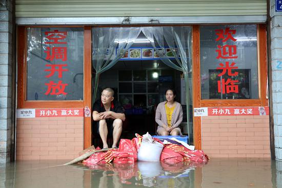 Owners of a small diner sit at the doorway as sandbags are used to hold off floodwaters in Suining, Sichuan Province, on Tuesday. (LIU CHANGSONG/FOR CHINA DAILY)