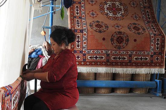 A woman weaves a carpet by hand at a local workshop in the Xinjiang Uygur autonomous region in May. (Photo by Li Lei/China Daily)
