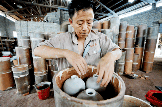 Craftsman Xiang Liping puts the porcelain embryo into the sagger, preparing it for burning. (Photo by Zhuo Zhongwei and Li Housheng/Asianewsphoto)