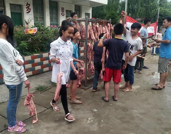 Students take home pork as an award at Zhiliao Primary School in Sanjiang county in the Guangxi Zhuang autonomous region on Friday. Those who scored over 80 in their Chinese and math final exams were awarded 1 kilogram of pork. The prize has been popular. (Photo/China News Service)