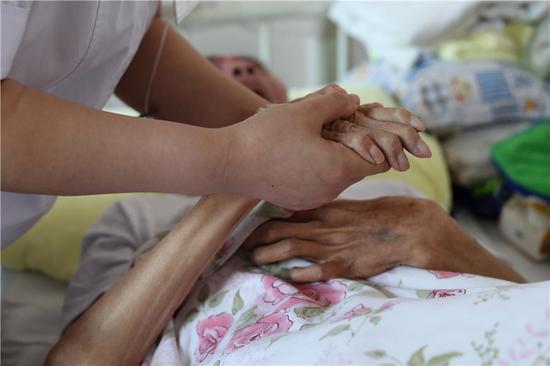 A staff member comforts a patient by holding his hands. (Photo: China Daily/Wang Jing)