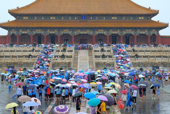 Visitors hold umbrellas in front of the Hall of Supreme Harmony at the Palace Museum, also known as the Forbidden City, in Beijing on Tuesday. Heavy rainfall hit the capital and led to road collapses in the city's suburbs. (LIU QIJIANG / FOR CHINA DAILY)