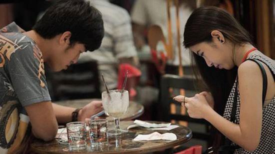 A young couple checks their mobile phones while having dinner. (File photo)