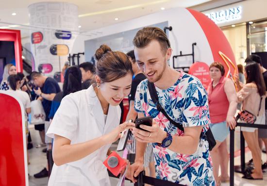 A shop assistant helps a foreign buyer pay on his mobile phone at a Tmall shop in Beijing. （Photo by Niu Jing/For China Daily）