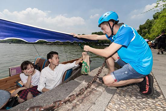 An Eleme delivery man hands Starbucks coffee to tourists at the West Lake in Hangzhou, Zhejiang Province. (Photo by Niu Jing/for China Daily)