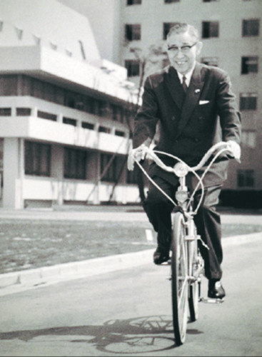 Konosuke Matsushita rides a bicycle at a Matsushita Electric factory. (Photo/Courtesy of Panasonic Corporation)