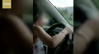A six-year-old girl drives while her dad sits in passenger's seat recording her. /Screenshot via CGTN