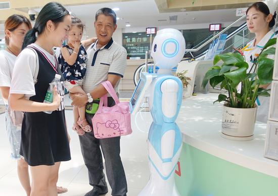 Visitors interact with a robot guide at Fuyang Women and Children Hospital in Fuyang, Anhui Province, on Aug. 2. (Photo by Wang Biao / For China Daily)