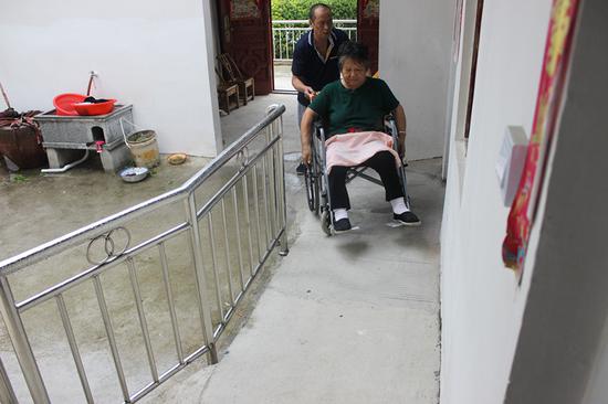 Yang Chuansheng pushes his wife along a ramp that makes it easier for them to enter and exit their house. (Photo/CHINA DAILY)
