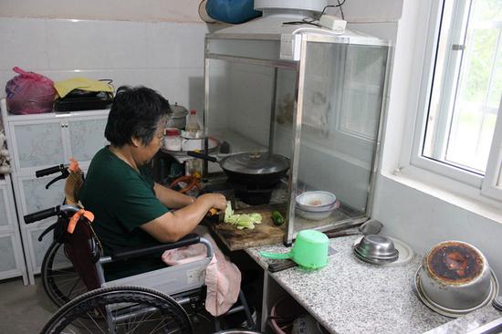 Ruan Guanqing, who is paralyzed from the waist down, uses low-level working surfaces to prepare food in Xinyang, Henan Province. (Photo/China Daily)