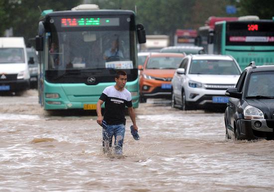 A man walks through a flooded street in Dalian, Liaoning Province, on Monday. Typhoon Rumbia brought torrential rains and caused severe flooding in the city. (LYU WENZHENG/FOR CHINA DAILY)