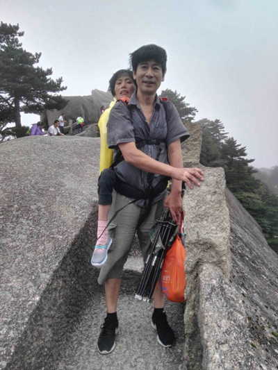 Wang Xiaomin carries his wife, Yu Yonghua, on his back at Huangshan Mountain in Anhui province. （Provided to China Daily）