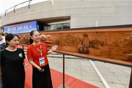 Liu Zao, owner of the Nashici Workshop, introduces Ode to the Silk Road, an 8.8-meter-long leather carving featuring deserts, camels, reclining Buddhas and architectural landmarks, at the opening ceremony of the ancient Silk Road tour in Beijing on Aug 28.(Photo by Zhu Xingxin/China Daily)