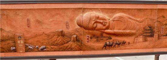 Liu Zao, owner of the Nashici Workshop, introduces Ode to the Silk Road, an 8.8-meter-long leather carving featuring deserts, camels, reclining Buddhas and architectural landmarks, at the opening ceremony of the ancient Silk Road tour in Beijing on Aug 28.(Photo by Zhu Xingxin/China Daily)