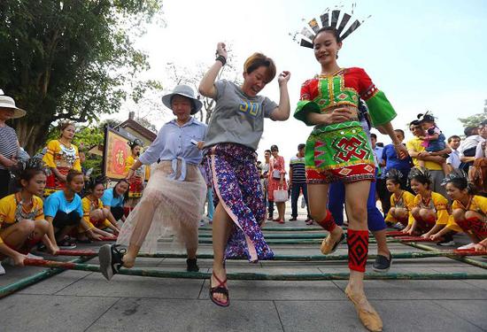 Tourists learn bamboo pole dancing at a tourism promotion event in Sanya, Hainan province. (Photo/Xinhua)
