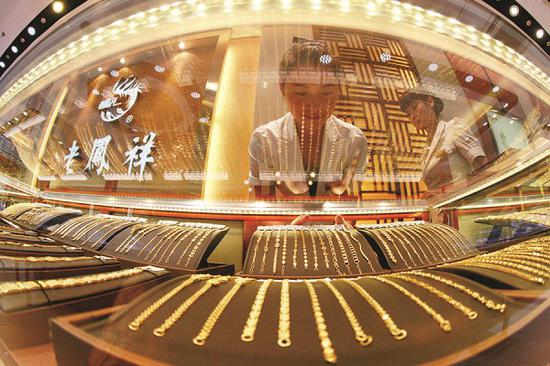 A saleswoman arranges gold jewelry at a Lao Feng Xiang store in Huaibei, Anhui province. (Photo by Xie Zhengyi/for China Daily)