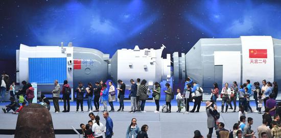 Visitors queue up to try out simulated games in front of a model of Tiangong-2 spacecraft at an aviation exhibition in Kunming, capital of Yunnan Province. (Photo/China News Service)