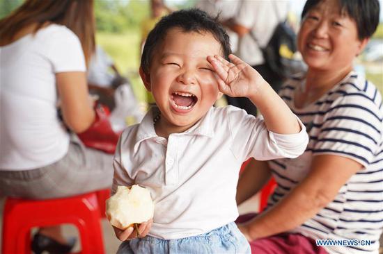 A smiling child eats pear at a pear planting base at Xiaogang Village in Fengyang County, east China's Anhui Province, on Sept. 15, 2018. (Xinhua/Cai Yang)