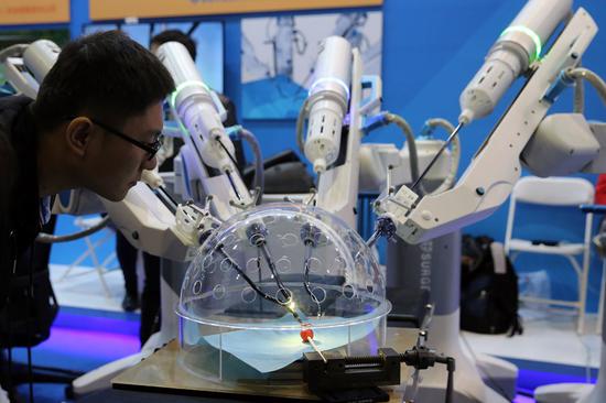 A visitor checks out a medical robot conducting simulated surgery on a grape at the opening of the Zhongguancun Innovation and Entrepreneurship Festival in Beijing. (Photo by Wang Zhuangfei/China Daily)