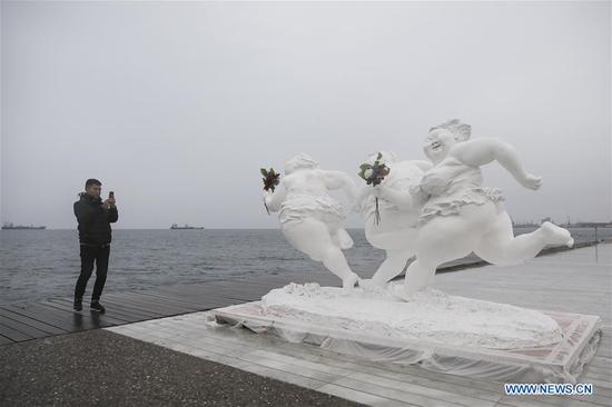 A man takes photos of a sculpture by Chinese artist Xu Hongfei at the port city of Thessaloniki, Greece, on Dec 18, 2018. （Photo/Xinhua）