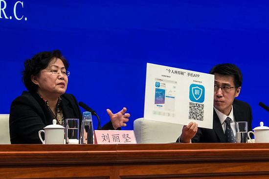 Liu Lijian (left), chief auditor of the State Administration of Taxation, and Luo Tianshu, director of the Department of Policy and Regulation at the tax authority, demonstrate how taxpayers can apply for income tax deductions via a mobile phone app at a news conference in Beijing on Monday. (Photo by HU YONGQI/CHINA DAILY)