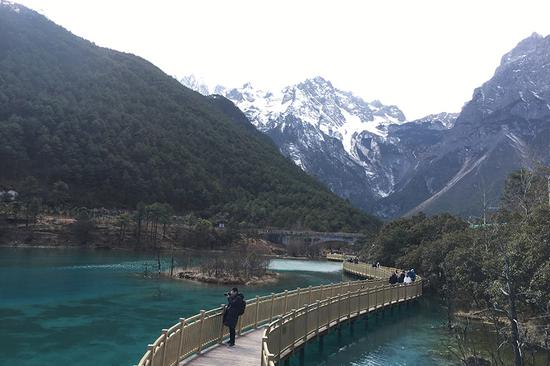 A tourist takes photo at the Blue Moon Valley, at the foot of Yulong Snow Mountain. The lake looks blue under sunlight. (PHOTO BY CHEN MEILING/CHINA DAILY)