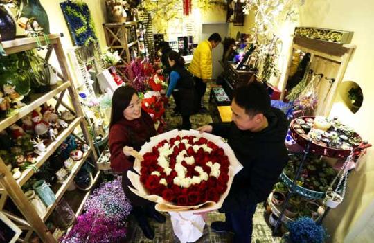 A flower shop staff member introduces flowers to a customer in Hengshui City, Hebei province February 12, 2017. （Photo/Xinhua）