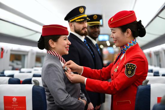 A train attendant helps foreign student trainees dress up in a car of a high-speed train about to depart from Xi'an, Shaanxi province, and bound for Beijing. (Photo by Tang Zhenjiang/for China Daily)