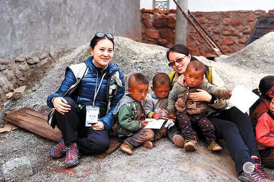 Emily Chan Yingyang (left) from the Chinese University of Hong Kong, and Du Wenwen of the Chinese Center for Disease Control and Prevention, pose with children in Hongyan village, Xide county, Sichuan province. (Photo by CCOUC/CHINA DAILY)