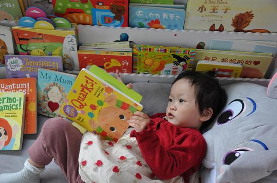 A one-year-old girl reads a book called Quarks. (Photo provided to China Daily)