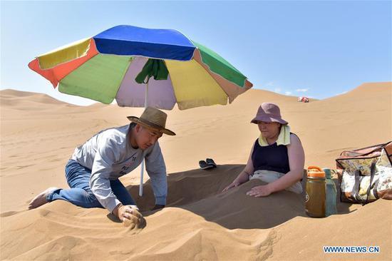 Tourists experience sand therapy in Kum Tag Desert of Xinjiang