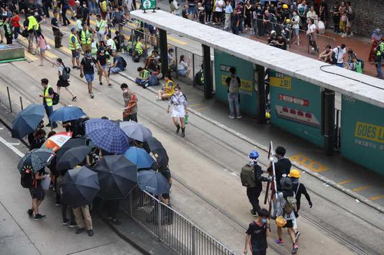 Sheltered by umbrellas, well-prepared protesters, in clear labor divisions, are dismantling metal barriers from the roadside in Causeway Bay, one of Hong Kong's business districts, on Sunday. [Photo/China Daily]