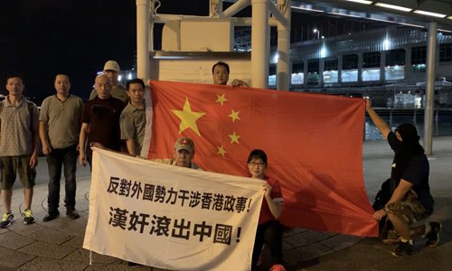 Patriotic Hong Kong residents pose for photos with the Chinese national flag at Hong Kong's Victoria Harbor on early Sunday morning. The banner reads 