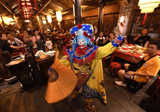 Customers watch a performance of bianlian, or face-changing－a feature of traditional Chinese opera that reveals a character's inner thoughts and feelings－at a hotpot restaurant in Chengdu, Sichuan province, earlier this month. LIU KUN/XINHUA
