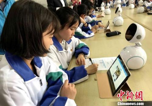 Students use a tablet PC to interact with a  robot in the classroom. (File photo/China News Service)